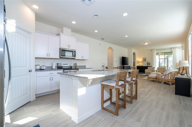 kitchen with light stone counters, a kitchen island with sink, white cabinets, appliances with stainless steel finishes, and sink