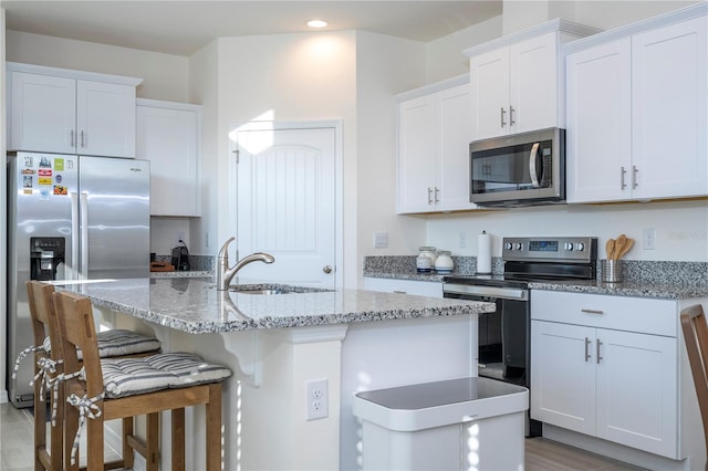 kitchen featuring an island with sink, appliances with stainless steel finishes, white cabinets, and a breakfast bar area