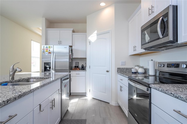 kitchen with stainless steel appliances, light stone countertops, white cabinets, and sink