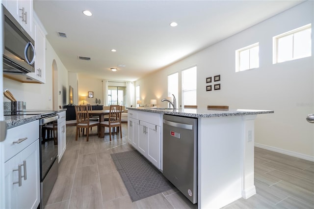 kitchen featuring light stone countertops, stainless steel appliances, white cabinetry, and a center island with sink