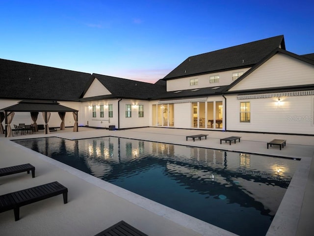 pool at dusk featuring a gazebo and a patio area