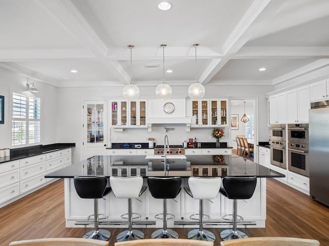 kitchen featuring beamed ceiling, a kitchen bar, coffered ceiling, and an island with sink