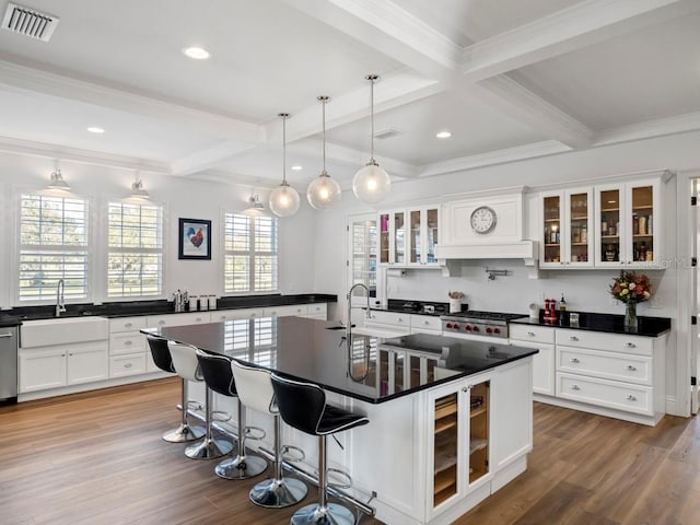 kitchen featuring beamed ceiling, sink, a kitchen breakfast bar, hanging light fixtures, and a kitchen island with sink