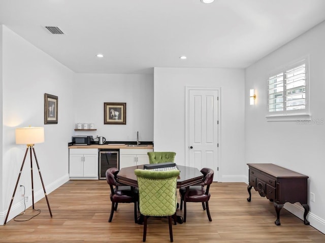 dining room featuring wet bar, wine cooler, and light hardwood / wood-style flooring