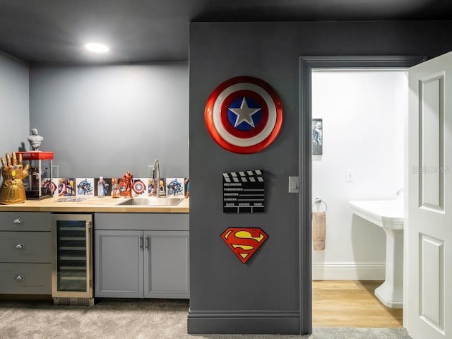 bar with sink, light colored carpet, beverage cooler, and gray cabinetry