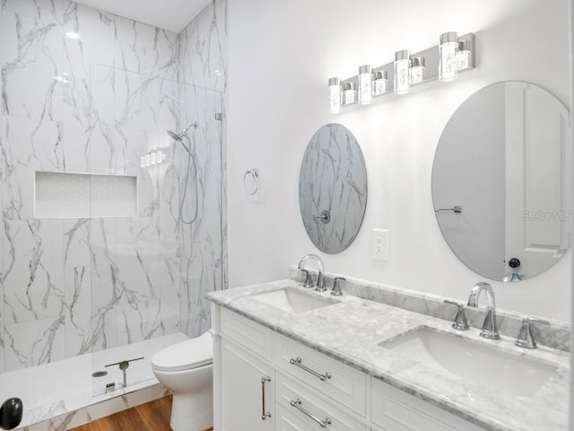 bathroom with toilet, vanity, wood-type flooring, and a tile shower