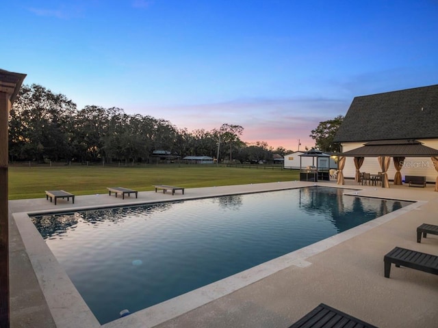 pool at dusk with a lawn, a gazebo, and a patio area