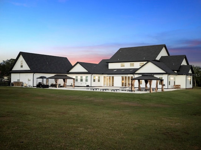 back house at dusk with a patio area, a gazebo, and a lawn