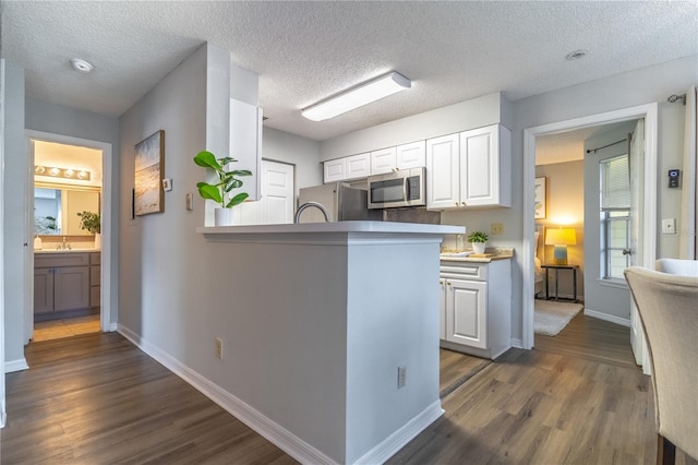 kitchen with fridge, dark hardwood / wood-style flooring, white cabinetry, and kitchen peninsula