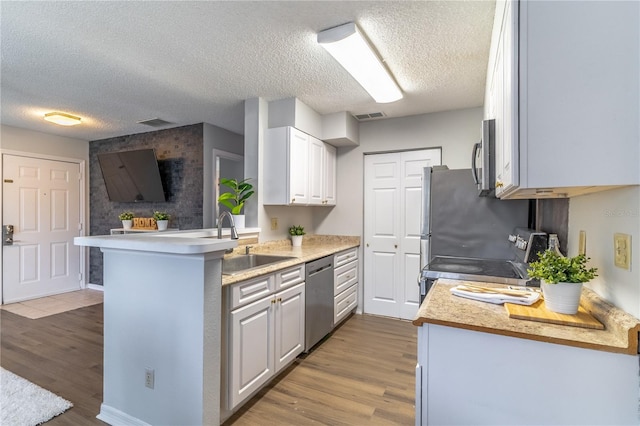 kitchen featuring dishwasher, kitchen peninsula, sink, white cabinetry, and stove