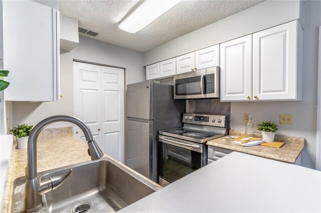 kitchen with stainless steel appliances, white cabinets, a textured ceiling, and sink