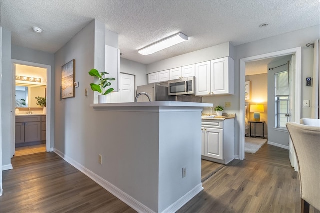 kitchen with stainless steel microwave, dark wood finished floors, white cabinets, fridge, and a textured ceiling