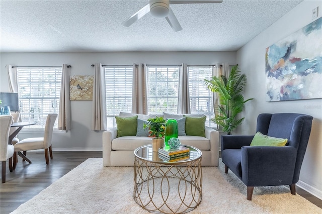 living area with wood finished floors, a ceiling fan, baseboards, and a textured ceiling