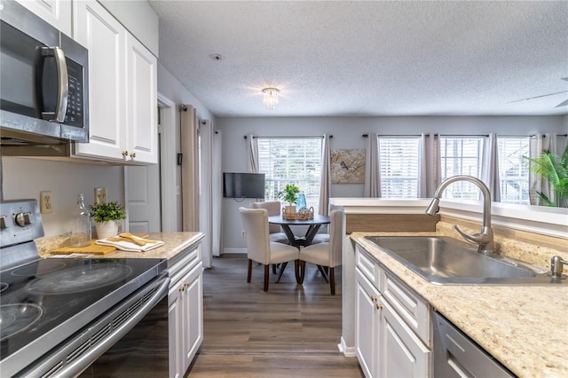 kitchen with appliances with stainless steel finishes, a sink, dark wood-type flooring, white cabinetry, and a textured ceiling