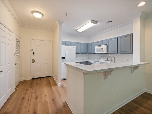 kitchen featuring a kitchen breakfast bar, light hardwood / wood-style floors, kitchen peninsula, and white appliances