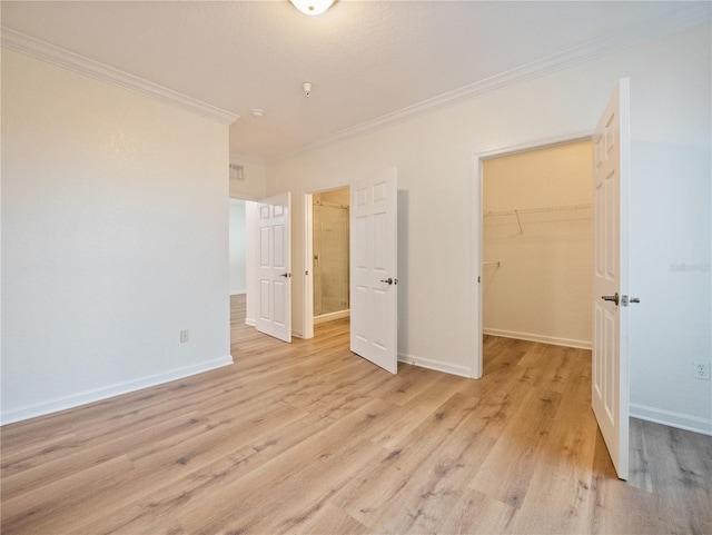 unfurnished bedroom with a spacious closet, a closet, ornamental molding, and light wood-type flooring