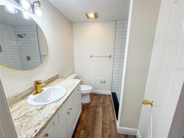 bathroom featuring toilet, hardwood / wood-style floors, tiled shower, a textured ceiling, and vanity