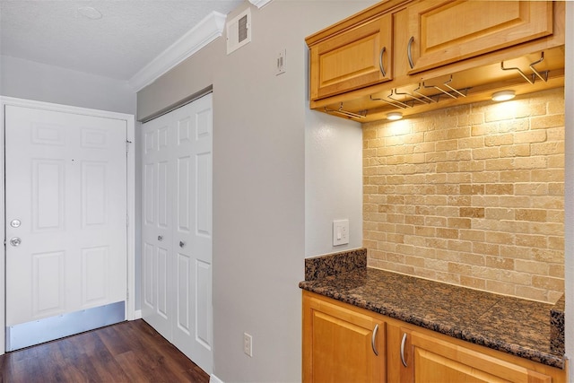 kitchen featuring a textured ceiling, visible vents, dark wood-style floors, dark stone countertops, and crown molding