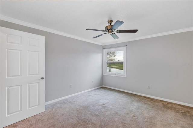 carpeted spare room featuring a ceiling fan, baseboards, and crown molding