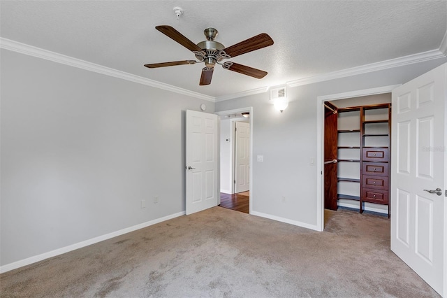 unfurnished bedroom with a walk in closet, visible vents, ornamental molding, carpet flooring, and baseboards