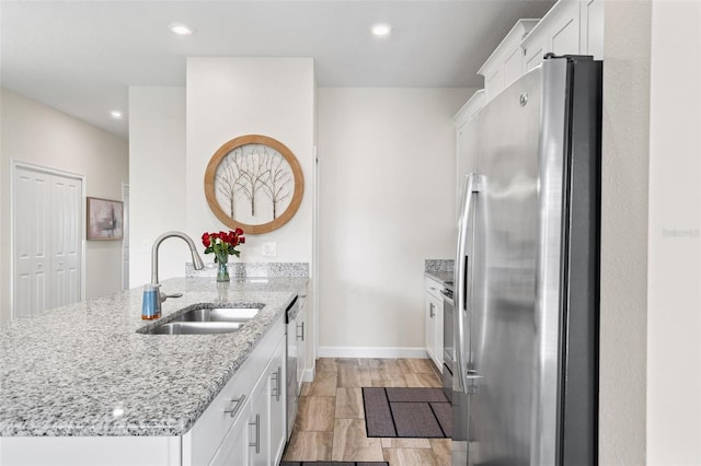 kitchen with stainless steel appliances, light stone countertops, white cabinetry, and sink