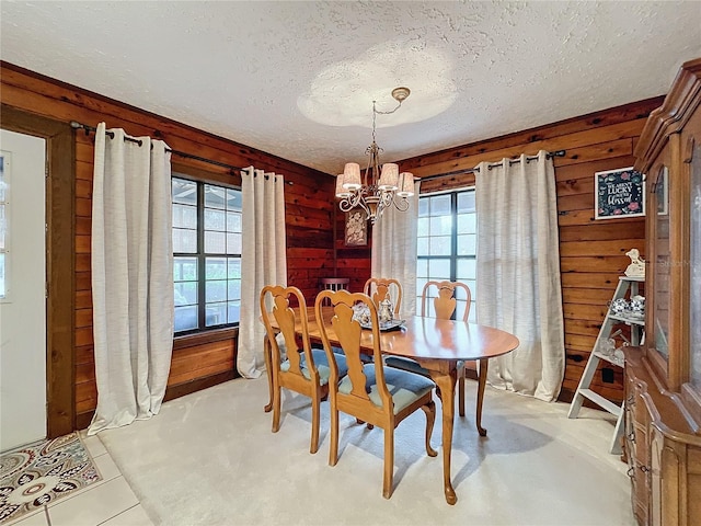 dining area with light tile patterned floors, a notable chandelier, wooden walls, and a textured ceiling