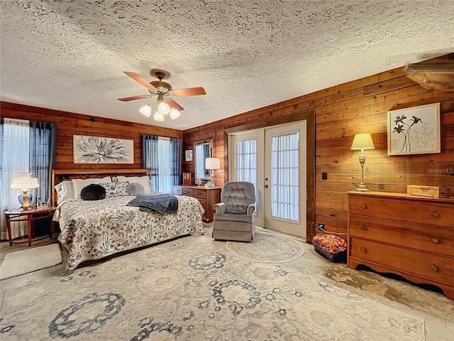 bedroom with ceiling fan, access to exterior, wooden walls, a textured ceiling, and french doors