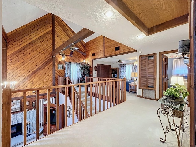 hall featuring a textured ceiling, carpet flooring, vaulted ceiling with beams, and wooden walls