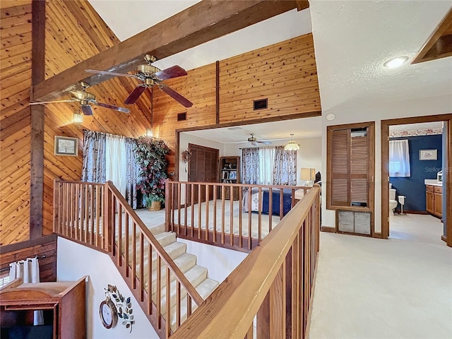 hallway with high vaulted ceiling, light colored carpet, beamed ceiling, and wooden walls