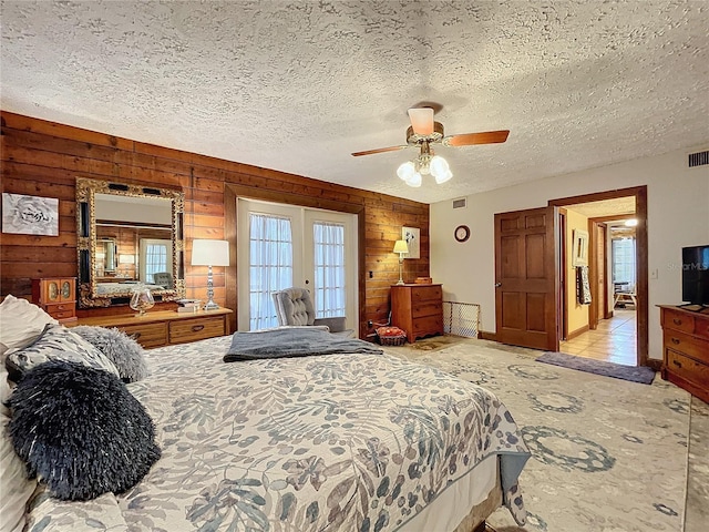 bedroom with a textured ceiling, ceiling fan, french doors, and wooden walls