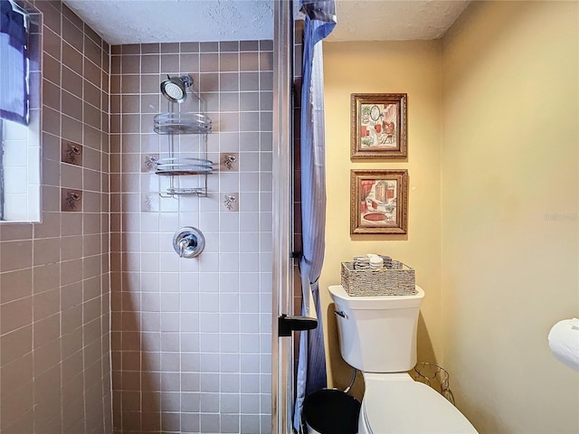 bathroom featuring a textured ceiling, toilet, and a tile shower