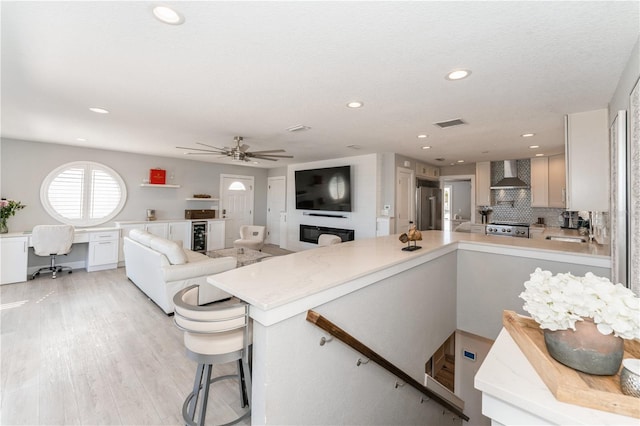 kitchen featuring kitchen peninsula, high end refrigerator, stove, wall chimney range hood, and built in desk