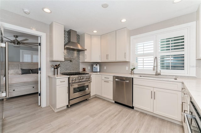 kitchen featuring sink, wall chimney range hood, stainless steel appliances, and white cabinetry