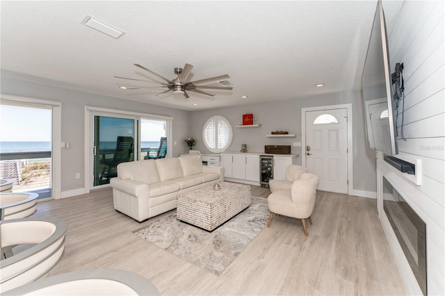 living room with a water view, a healthy amount of sunlight, ceiling fan, and beverage cooler