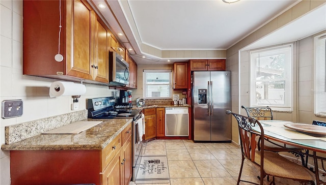 kitchen featuring light stone countertops, crown molding, light tile patterned floors, and stainless steel appliances