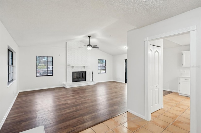 unfurnished living room with ceiling fan, lofted ceiling, a brick fireplace, a textured ceiling, and light tile patterned floors