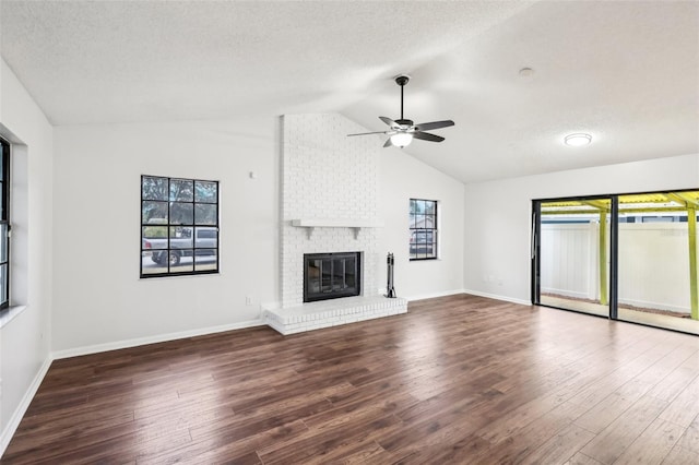 unfurnished living room with a brick fireplace, ceiling fan, dark wood-type flooring, lofted ceiling, and a textured ceiling