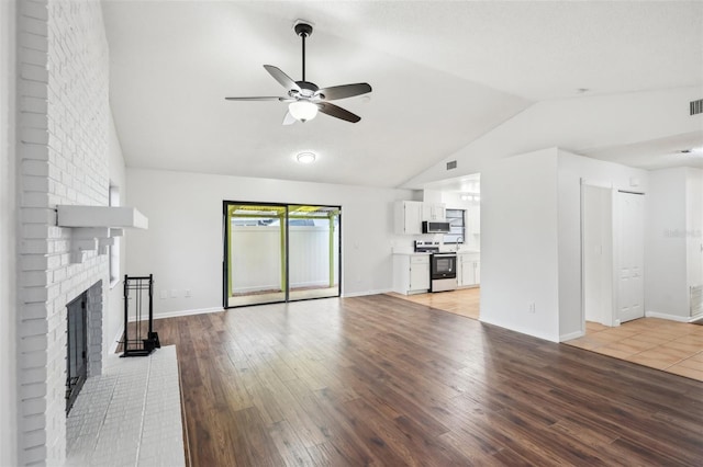 unfurnished living room with lofted ceiling, ceiling fan, a brick fireplace, and light wood-type flooring