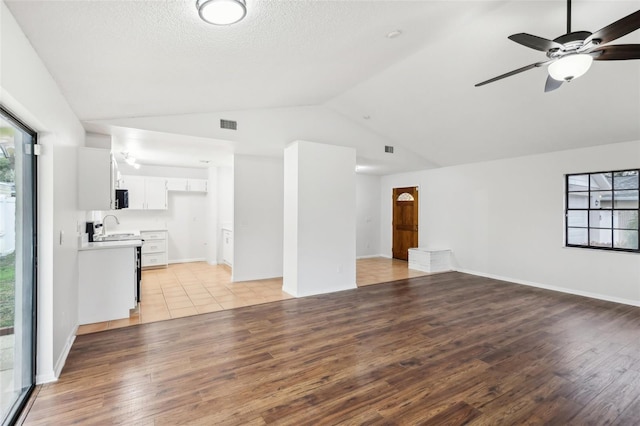 unfurnished living room with a textured ceiling, ceiling fan, lofted ceiling, and light hardwood / wood-style flooring