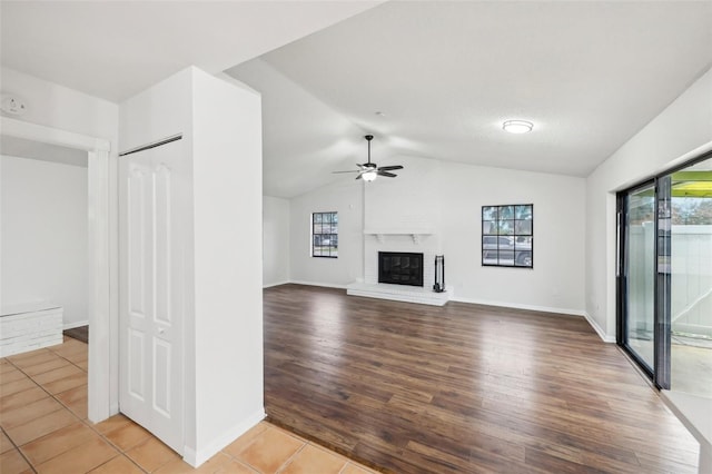 unfurnished living room with ceiling fan, tile patterned floors, a brick fireplace, and vaulted ceiling