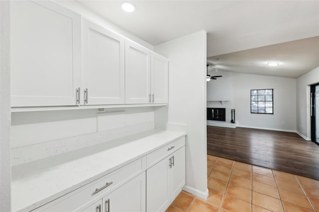 interior space featuring light tile patterned flooring, white cabinets, ceiling fan, vaulted ceiling, and a brick fireplace