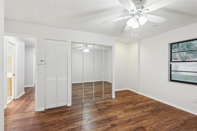 unfurnished bedroom featuring ceiling fan, dark hardwood / wood-style flooring, a textured ceiling, and two closets