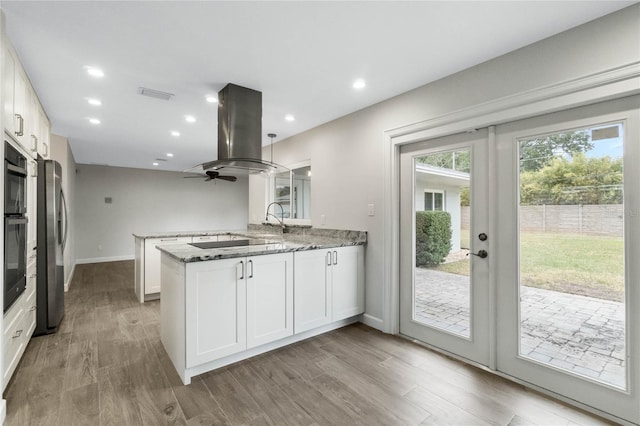 kitchen featuring island range hood, kitchen peninsula, dark stone countertops, white cabinets, and black appliances