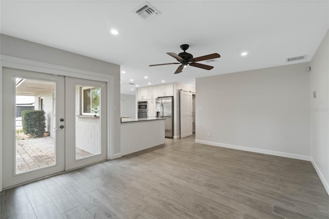 unfurnished living room with light wood-type flooring, ceiling fan, and french doors