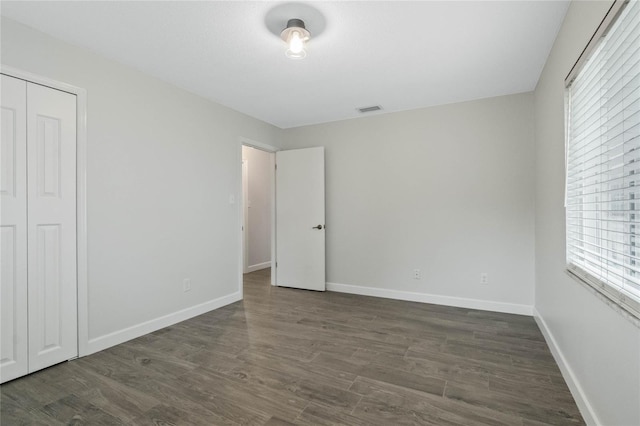 unfurnished bedroom featuring a closet, dark hardwood / wood-style floors, and multiple windows