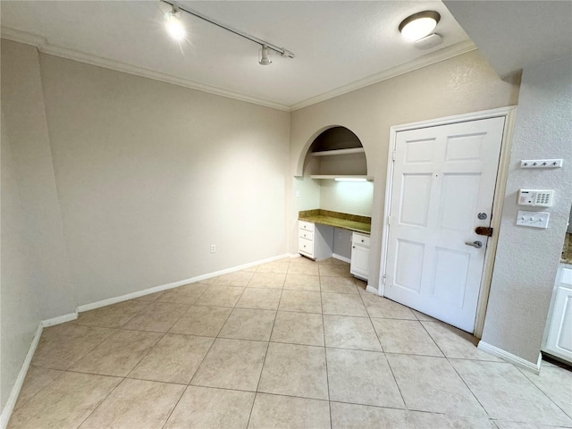 unfurnished room featuring baseboards, built in features, crown molding, built in desk, and light tile patterned flooring