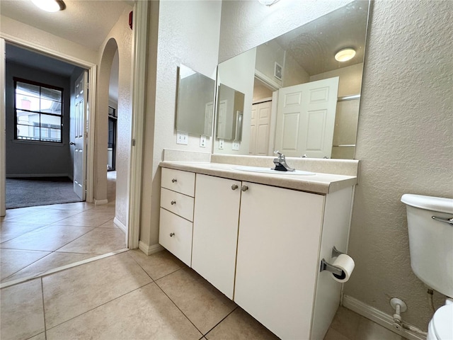 full bath with baseboards, a textured wall, toilet, tile patterned flooring, and vanity