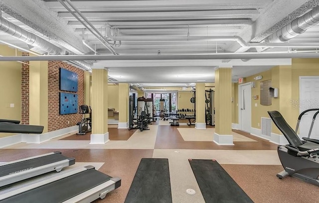 gym featuring baseboards, visible vents, and brick wall