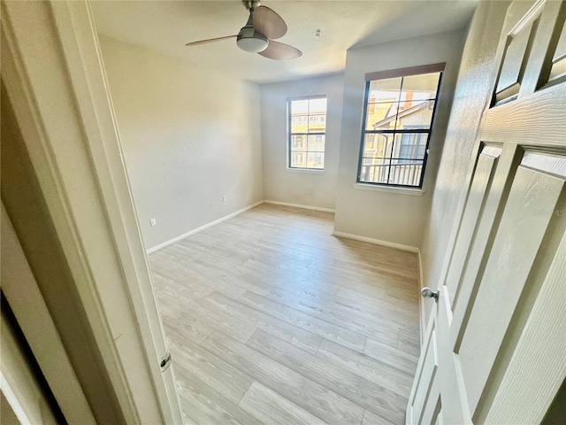 spare room featuring a ceiling fan, baseboards, and light wood finished floors