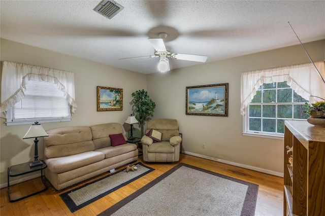 living room with a textured ceiling, ceiling fan, and light wood-type flooring